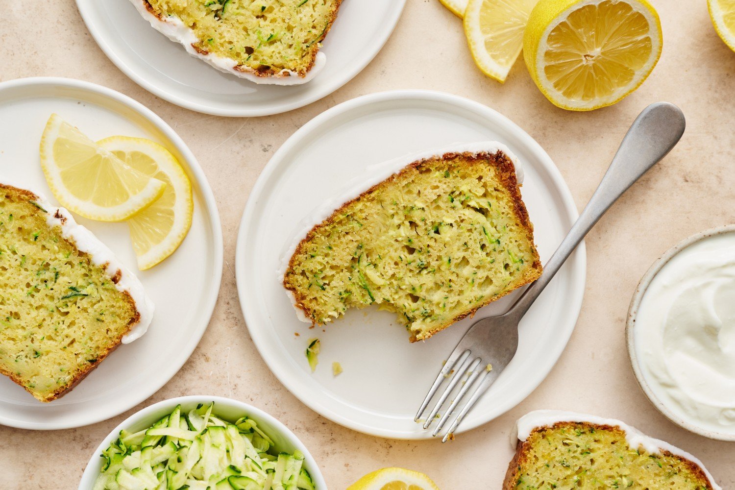 slices of lemon yogurt zucchini bread on a plate with forks, with one slice with a bite taken out.