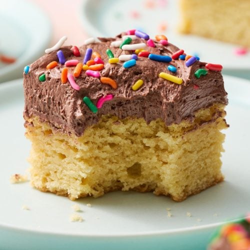 a slice of sugar cookie bar on a plate with chocolate frosting and sprinkles on top, with a bite taken out.