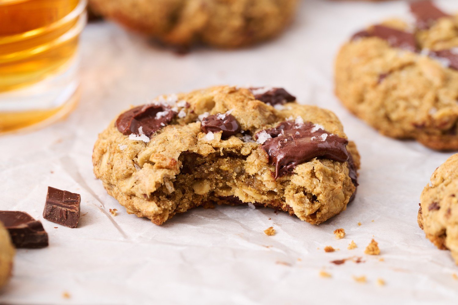 a single Bourbon Rye Oatmeal Chocolate Chunk Cookie with a bite taken out, and a few more cookies scattered in the background.