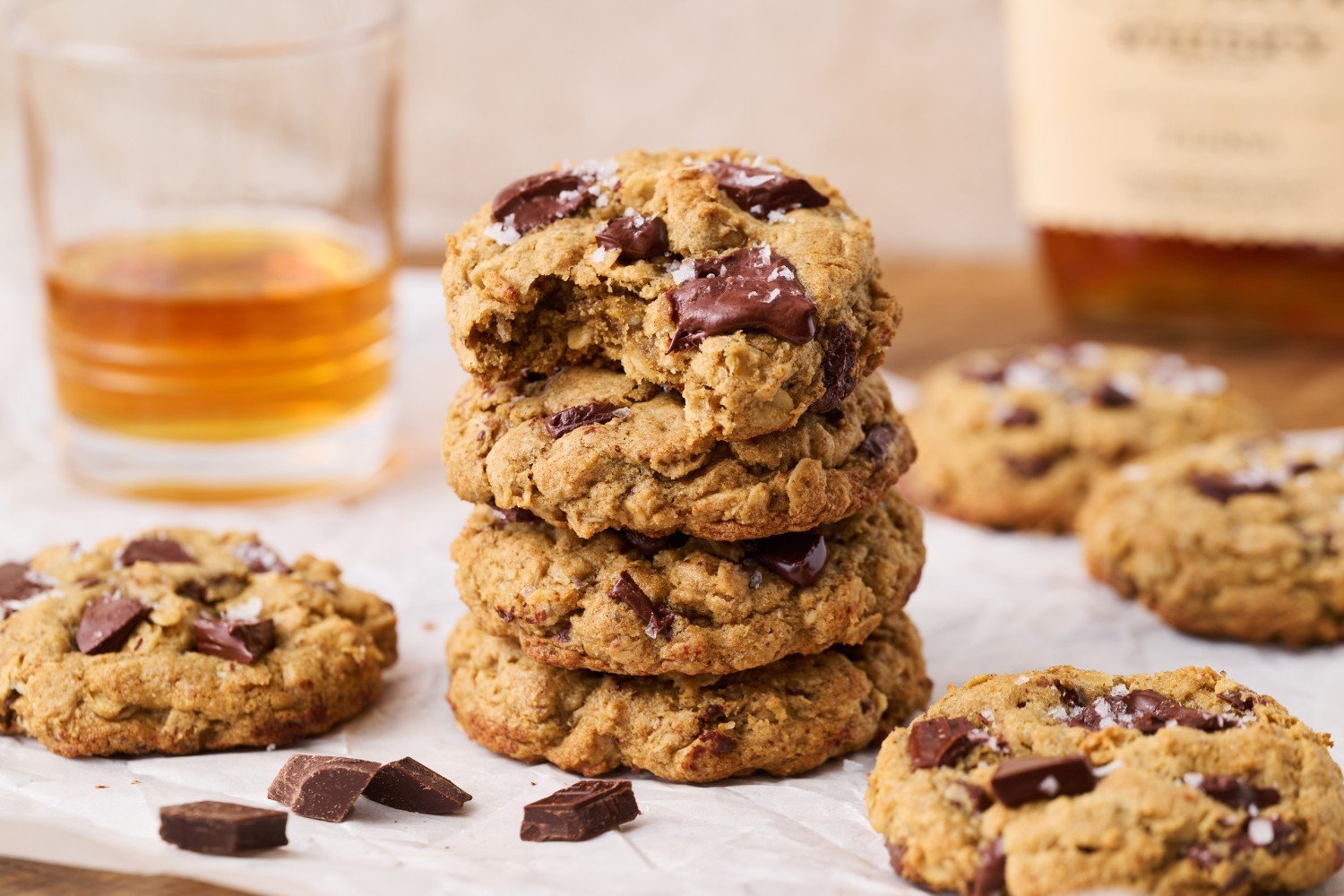 a stack of bourbon cookies with one cookie with a bite taken out, and a glass of bourbon in the background.