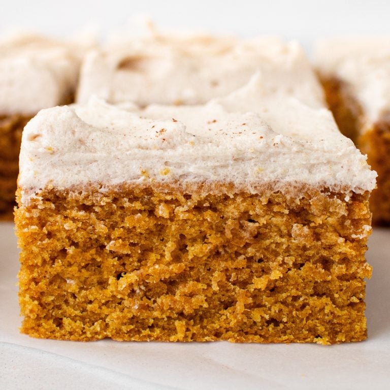 a slice of pumpkin bar with brown sugar frosting with more pumpkin bars in the background.