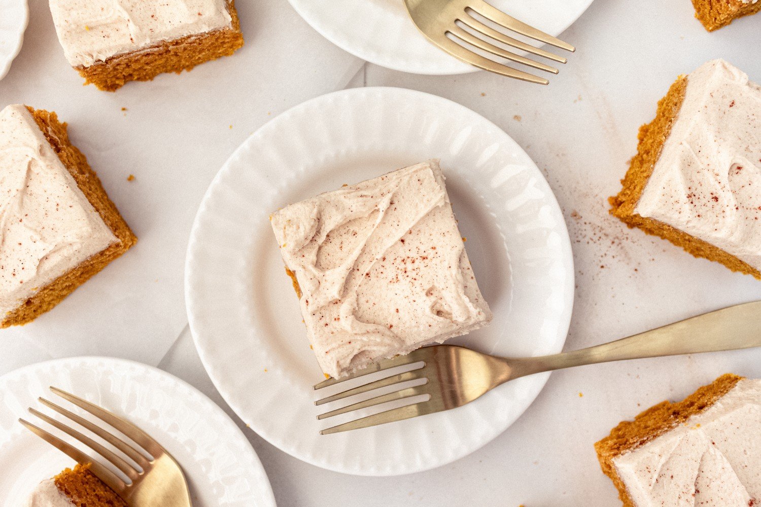 slices of frosted pumpkin bars on white plates with forks, ready to serve.