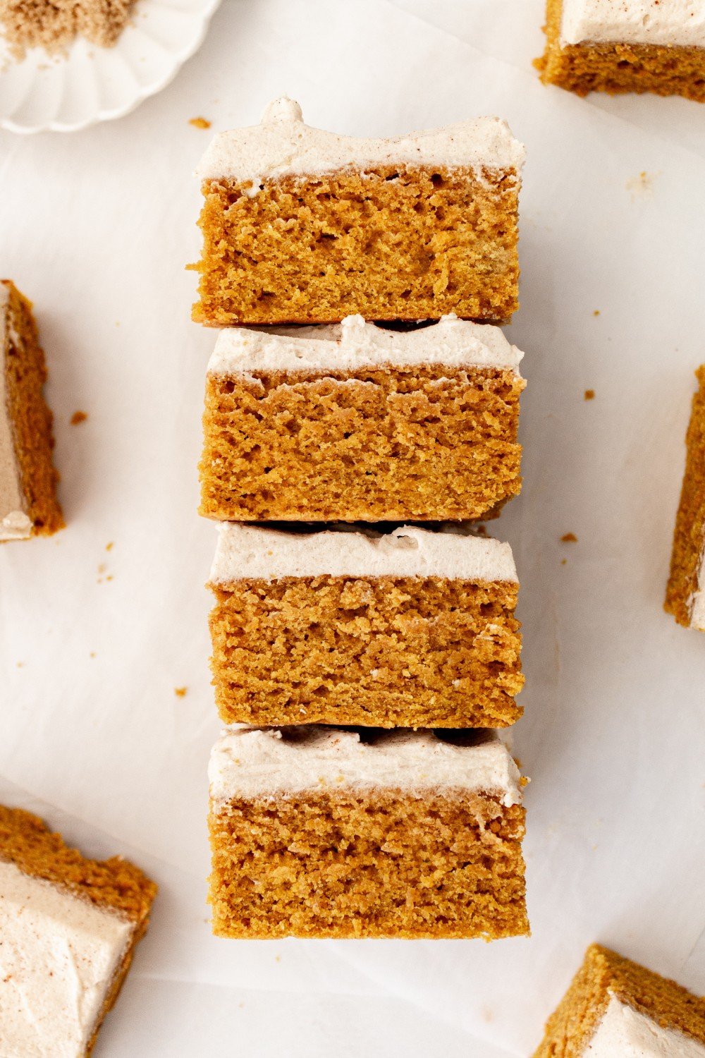 four pumpkin bars with brown sugar frosting stacked on a white background.