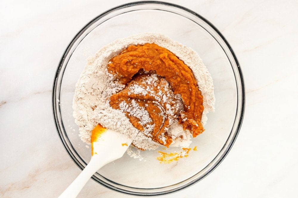 clear bowl with dry ingredients mixing with wet ingredients for pumpkin bars
