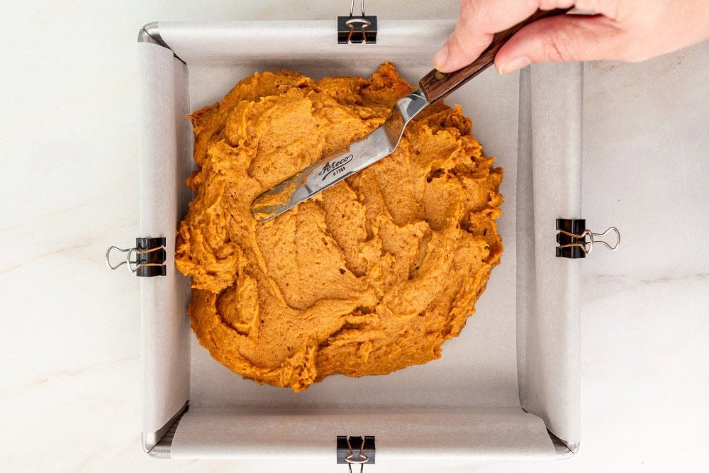 pumpkin bar batter being spread into parchment-lined square pan