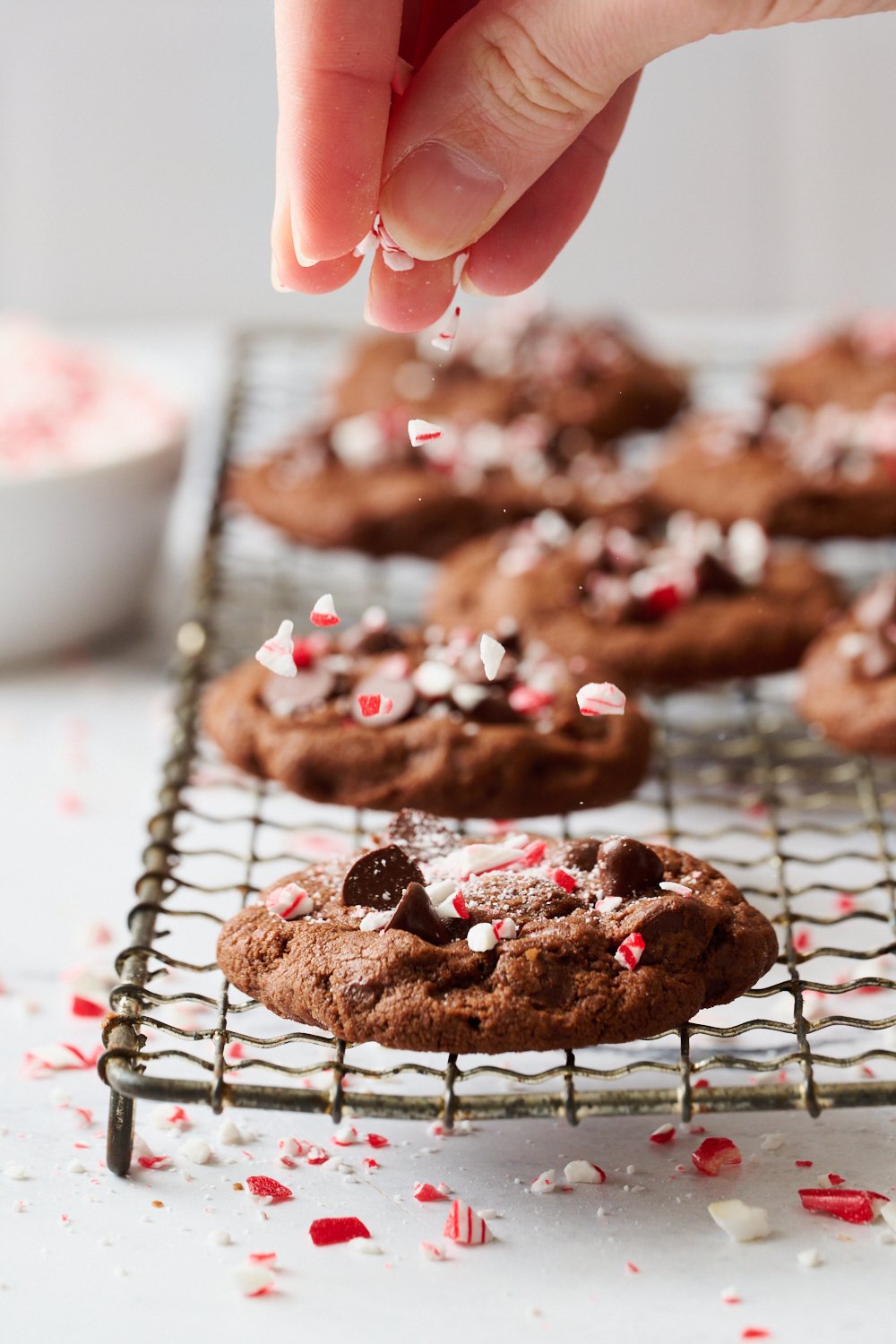 several cookies on a cooling rack, being sprinkled with crushed candy canes.