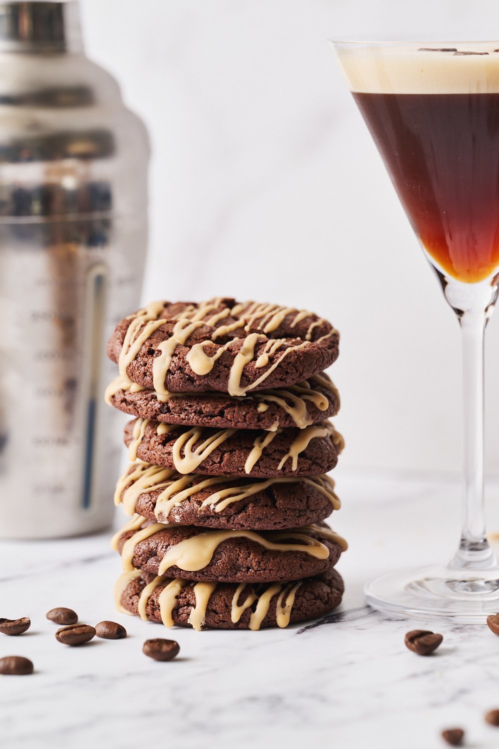 a stack of several espresso martini cookies, with an espresso martini cocktail and a cocktail shaker in the background. 