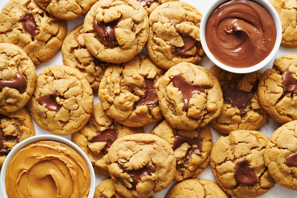 a whole batch of peanut butter nutella cookies with bowls of peanut butter and nutella nearby.