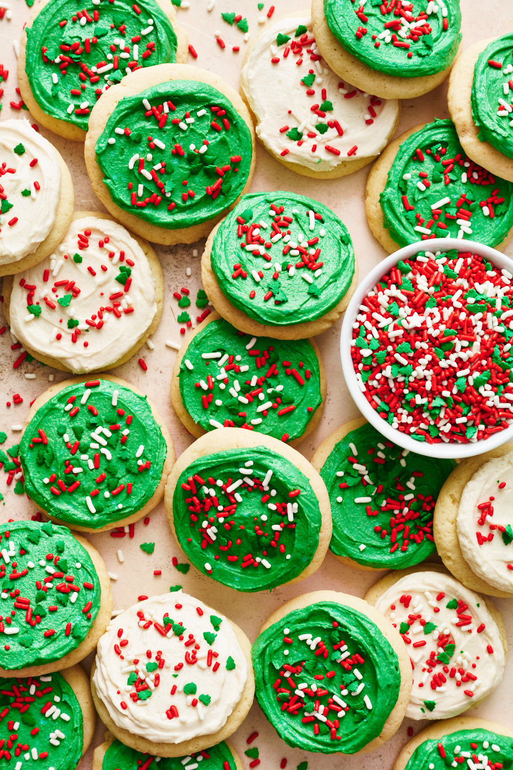 the whole batch of Christmas Lofthouse Cookies on brown parchment paper, with a bowl of sprinkles to the side.