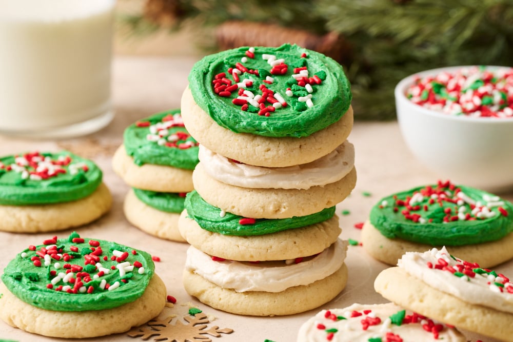 a stack of cookies with more cookies and a bowl of sprinkles in the background.