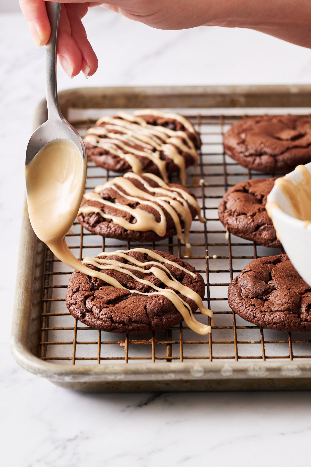 the glaze being drizzled on top of baked, cooled cookies using a spoon.