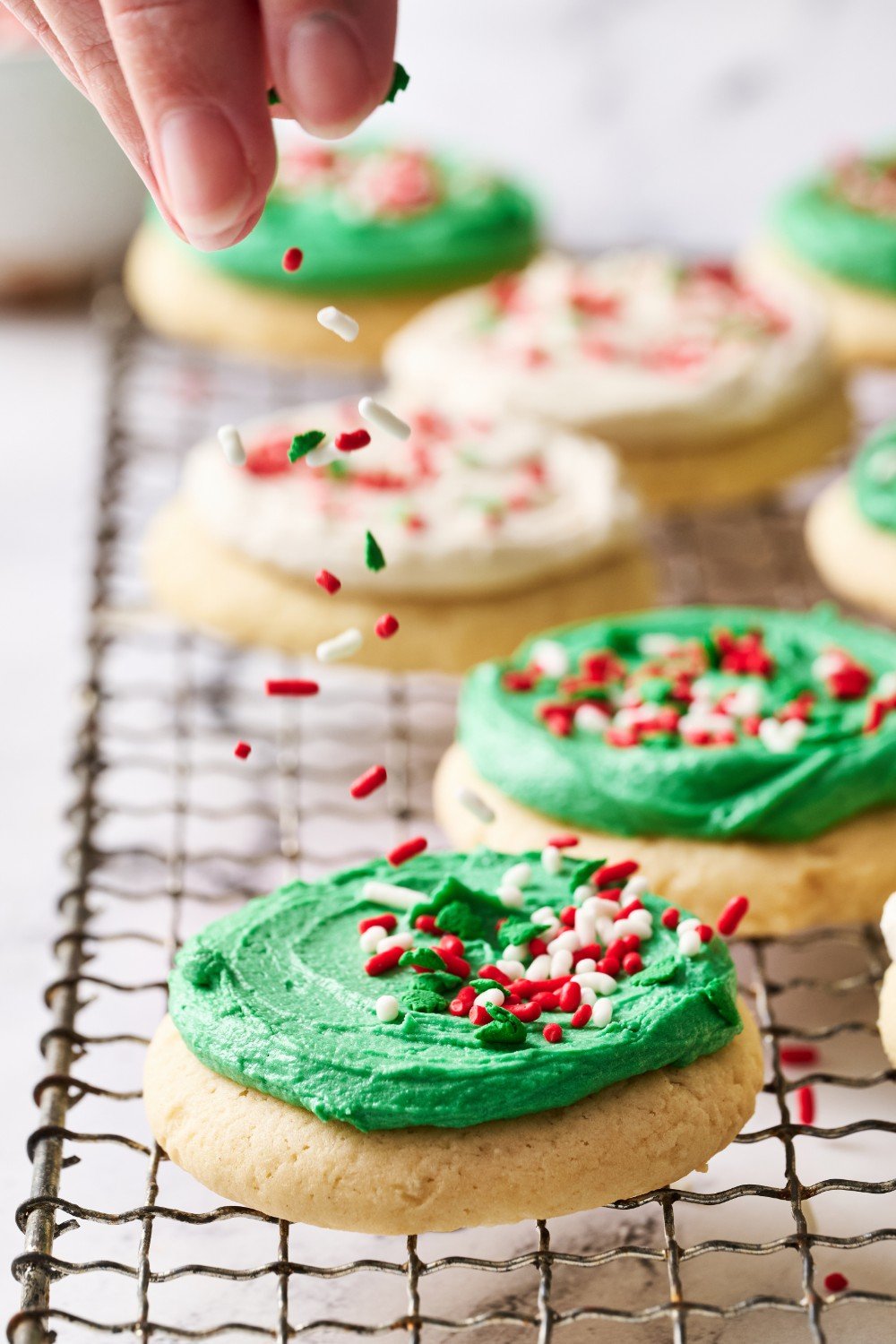 a hand sprinkling the top of an iced cookie with sprinkles.