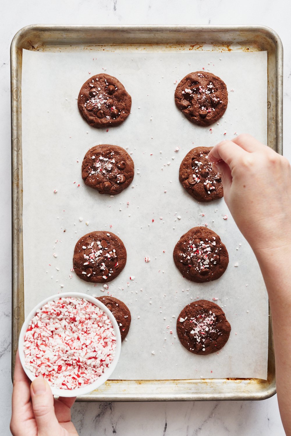 a tray of peppermint chocolate cookies being sprinkled with crushed candy canes straight out of the oven.