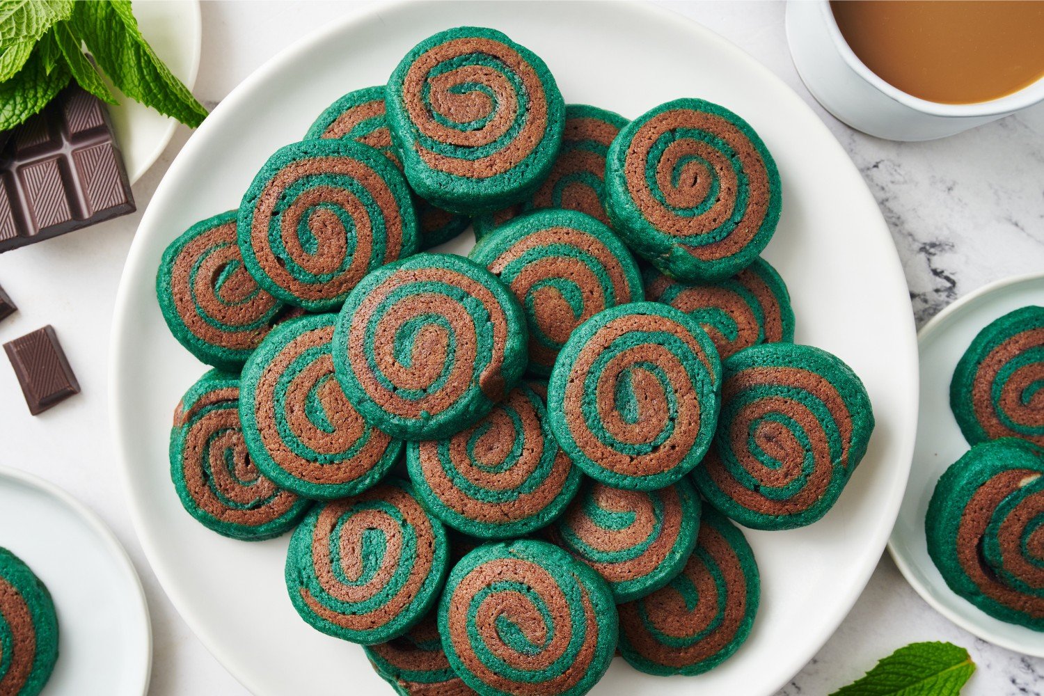 white platter full of cookies, surrounded by a cup of coffee and fresh mint.