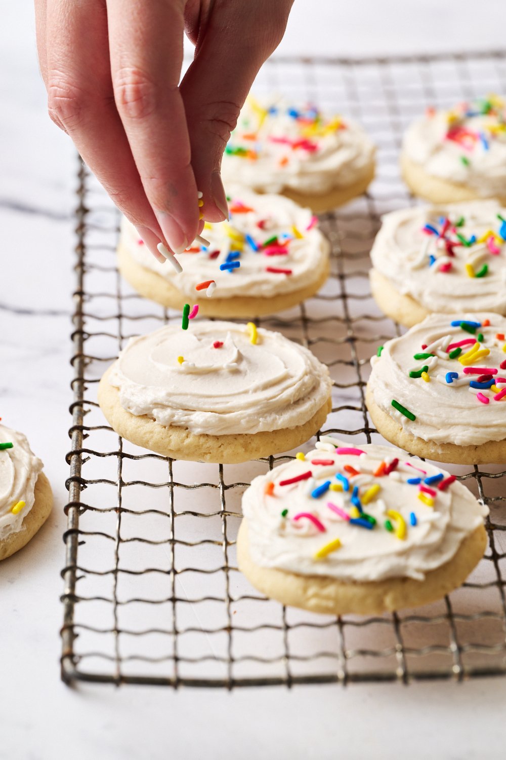 an iced Lofthouse Sugar Cookie with rainbow sprinkles being added before the icing sets.