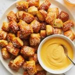 a large white platter full of salt-topped soft pretzel bites, with a bowl of beer cheese dip.