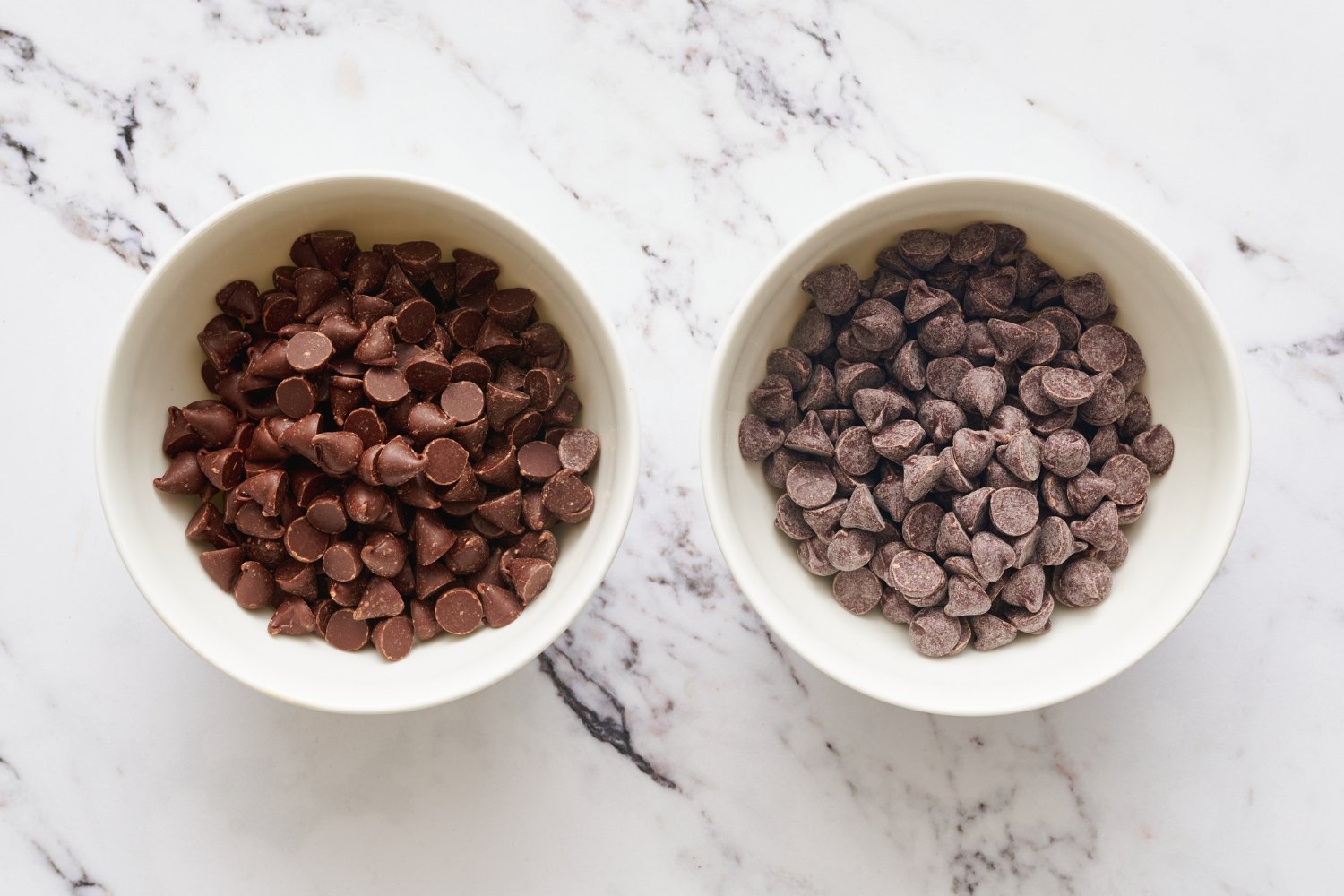 two white ramekins, one filled with fresh chocolate chips, and the other filled with bloomed chocolate chips, both on a marble surface. 