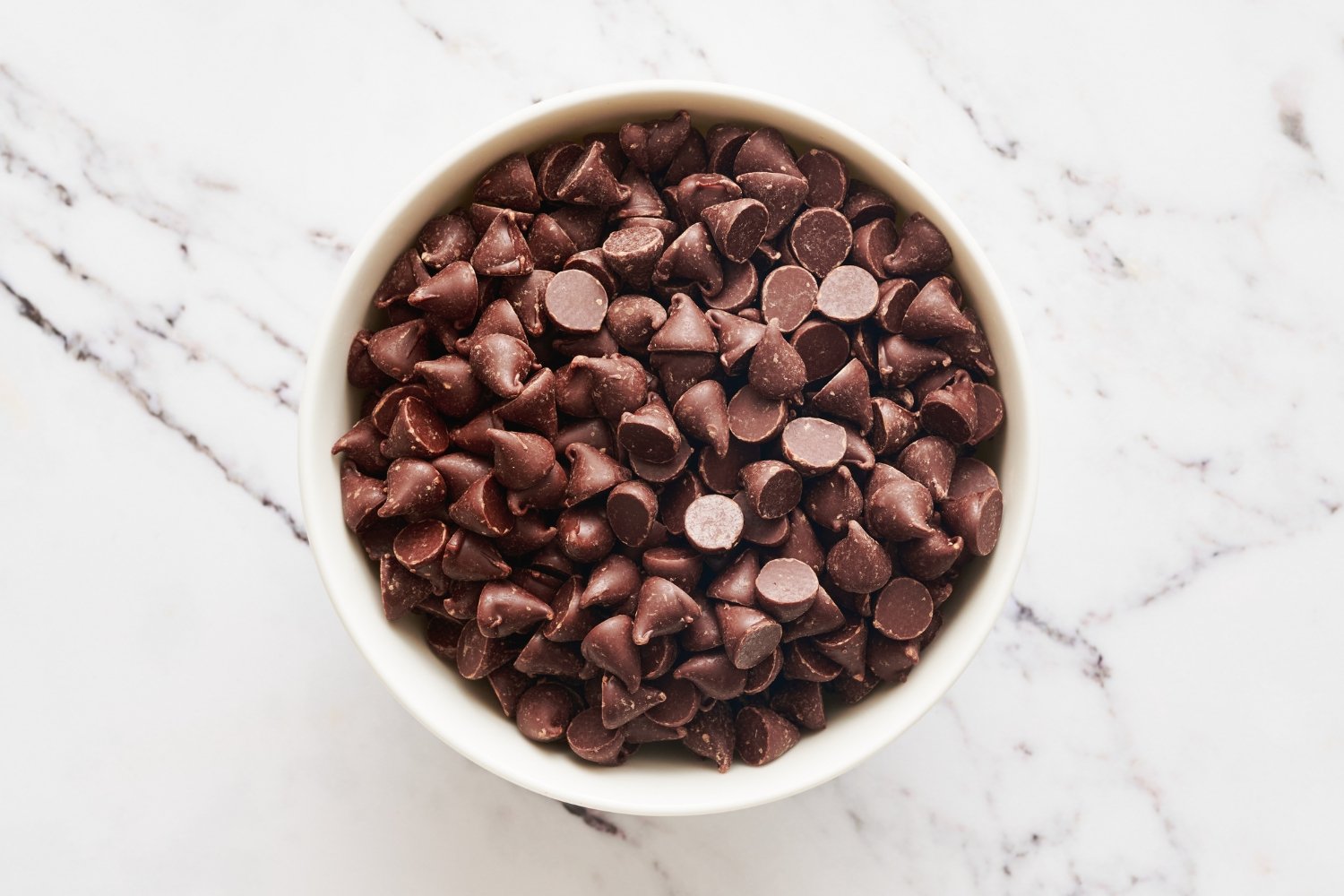 a small white ramekin filled with chocolate chips on a marble surface. 