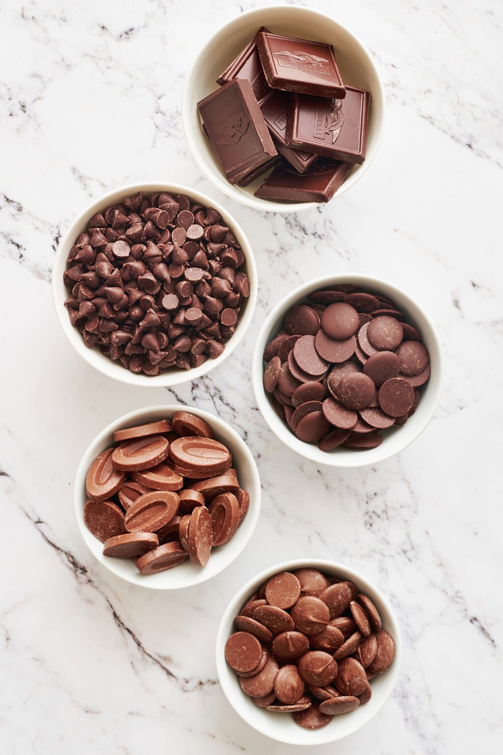 several types of decorating and baking chocolate in small white bowls on a marble surface.