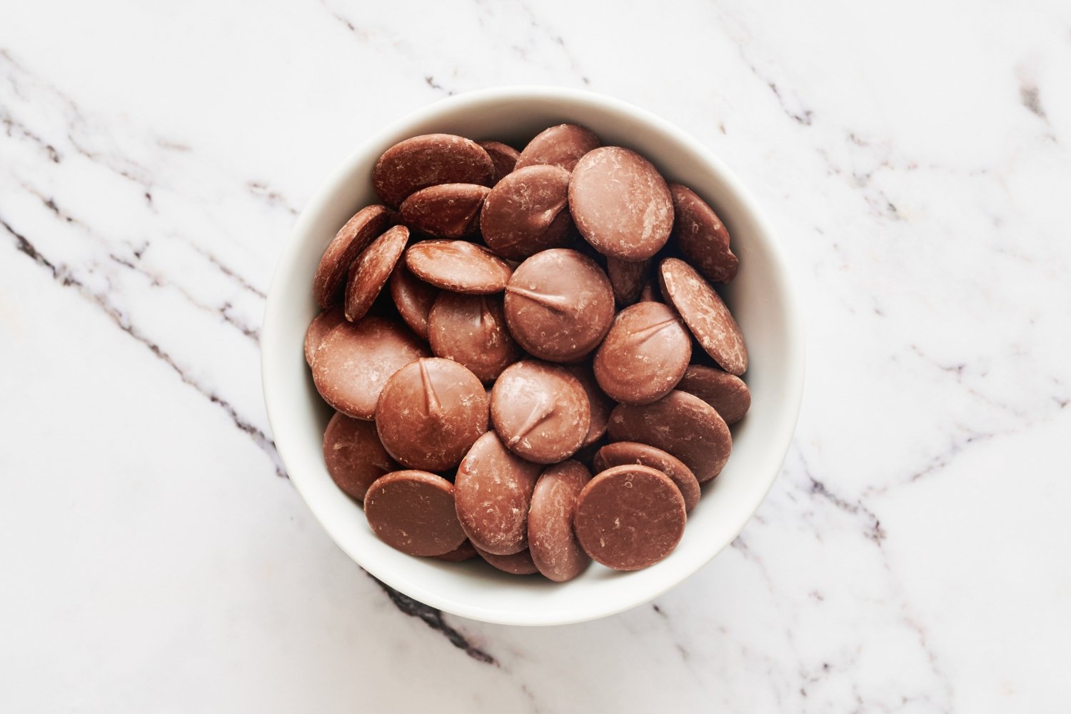 a small white ramekin filled with coating chocolate pieces on a marble surface. 