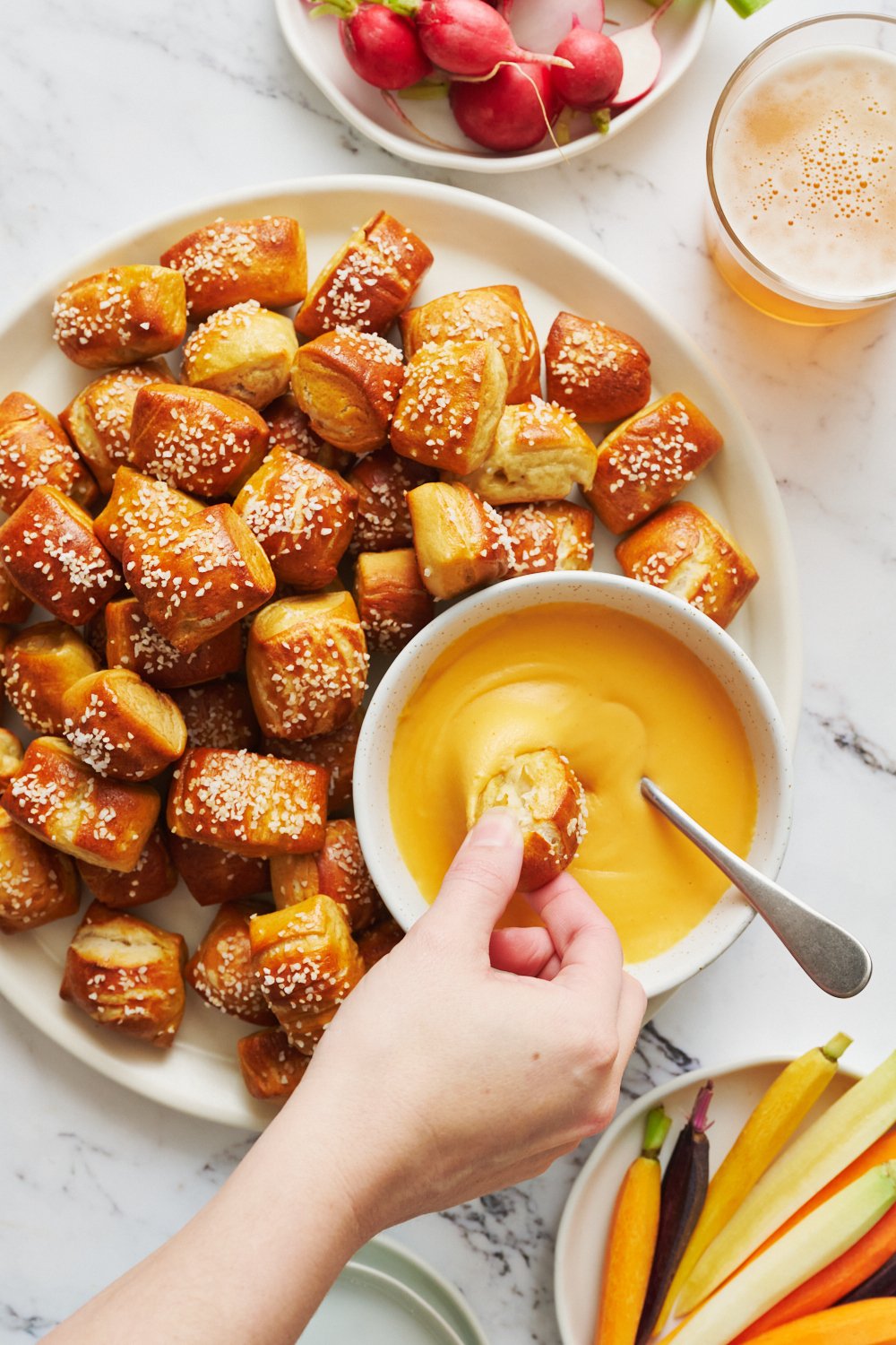 a hand dipping a soft pretzel bite in beer cheese.