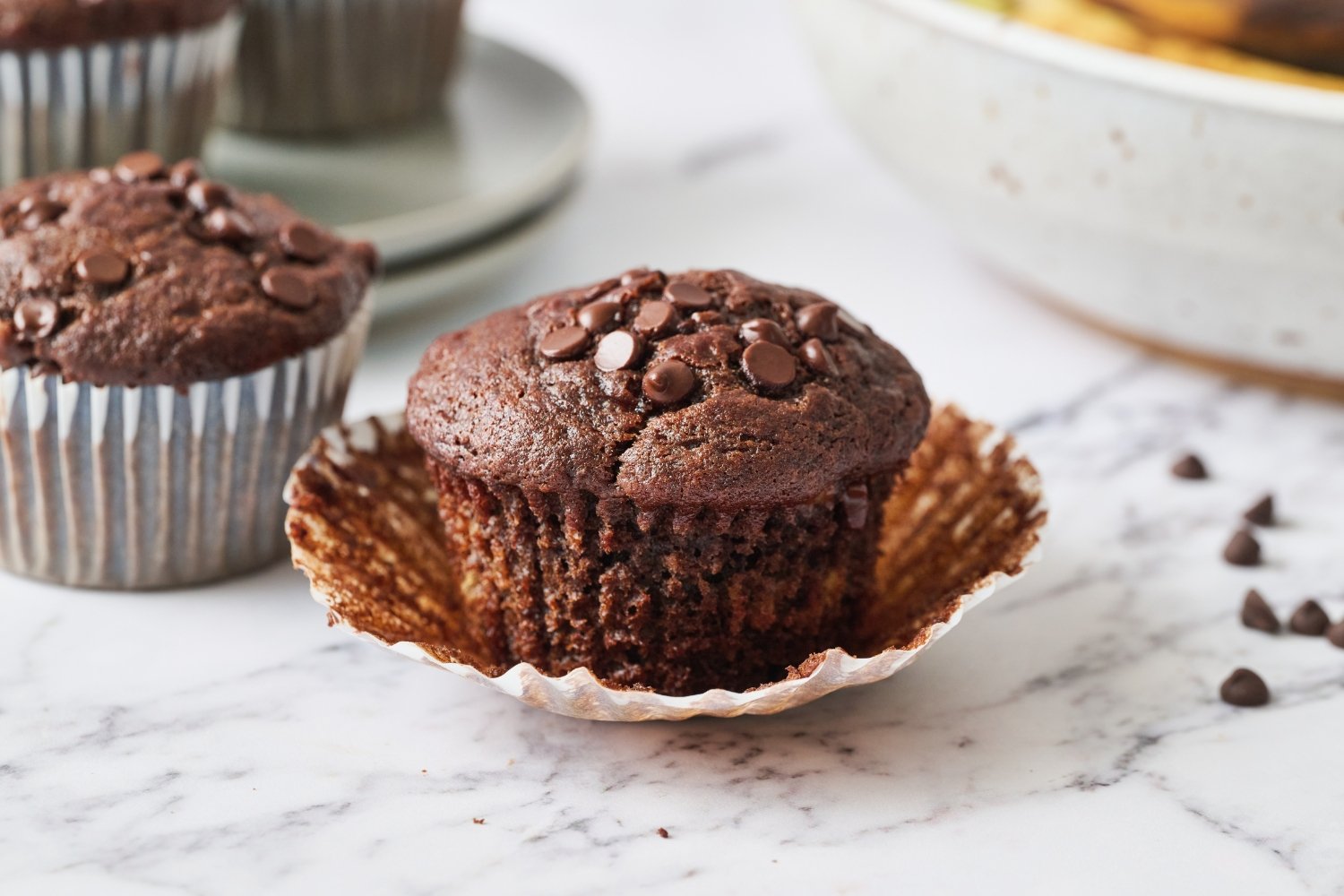 a double chocolate banana muffin on a marble surface with the paper liner being removed.