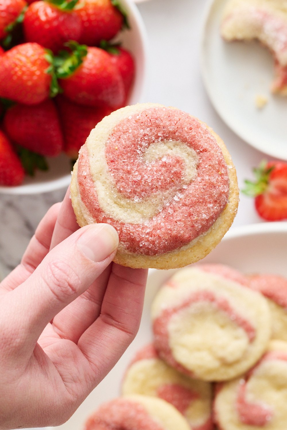 a strawberry cookie held above a plate of more cookies and fresh berries.