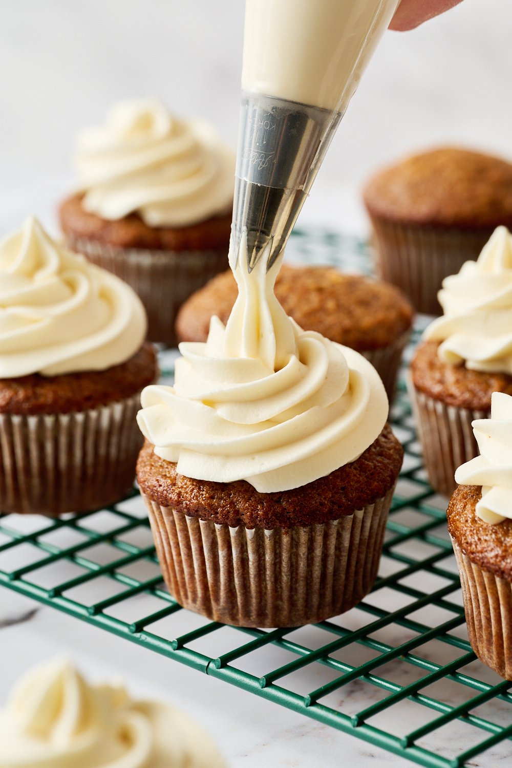 cream cheese frosting being piped on top of a cooled cupcake.