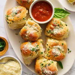 several garlic knot rolls on a white platter with a small bowl of marinara sauce.