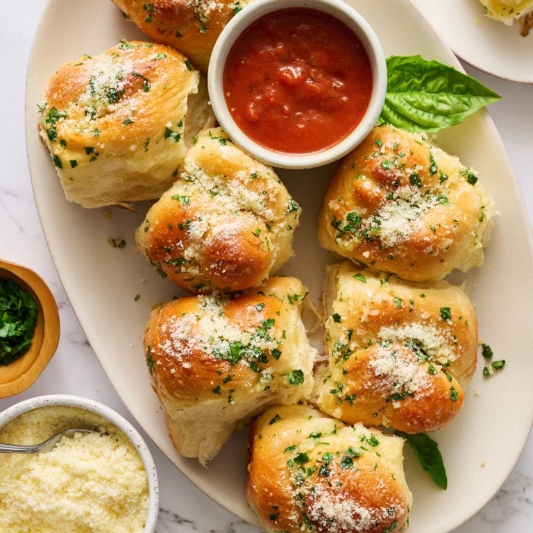 several garlic knot rolls on a white platter with a small bowl of marinara sauce.