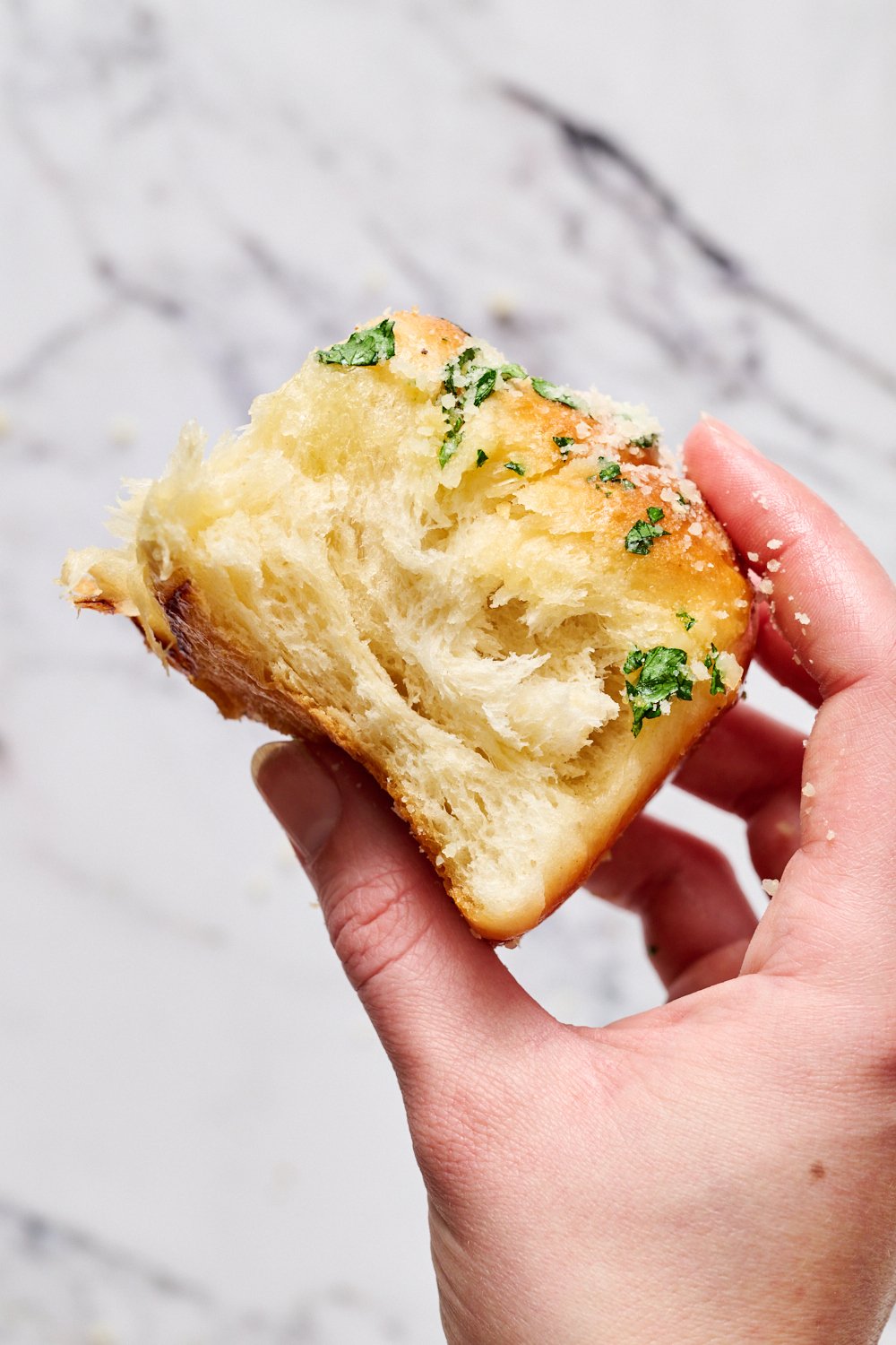 a hand holding a garlic knot roll, covered in garlic butter and Parmesan cheese.