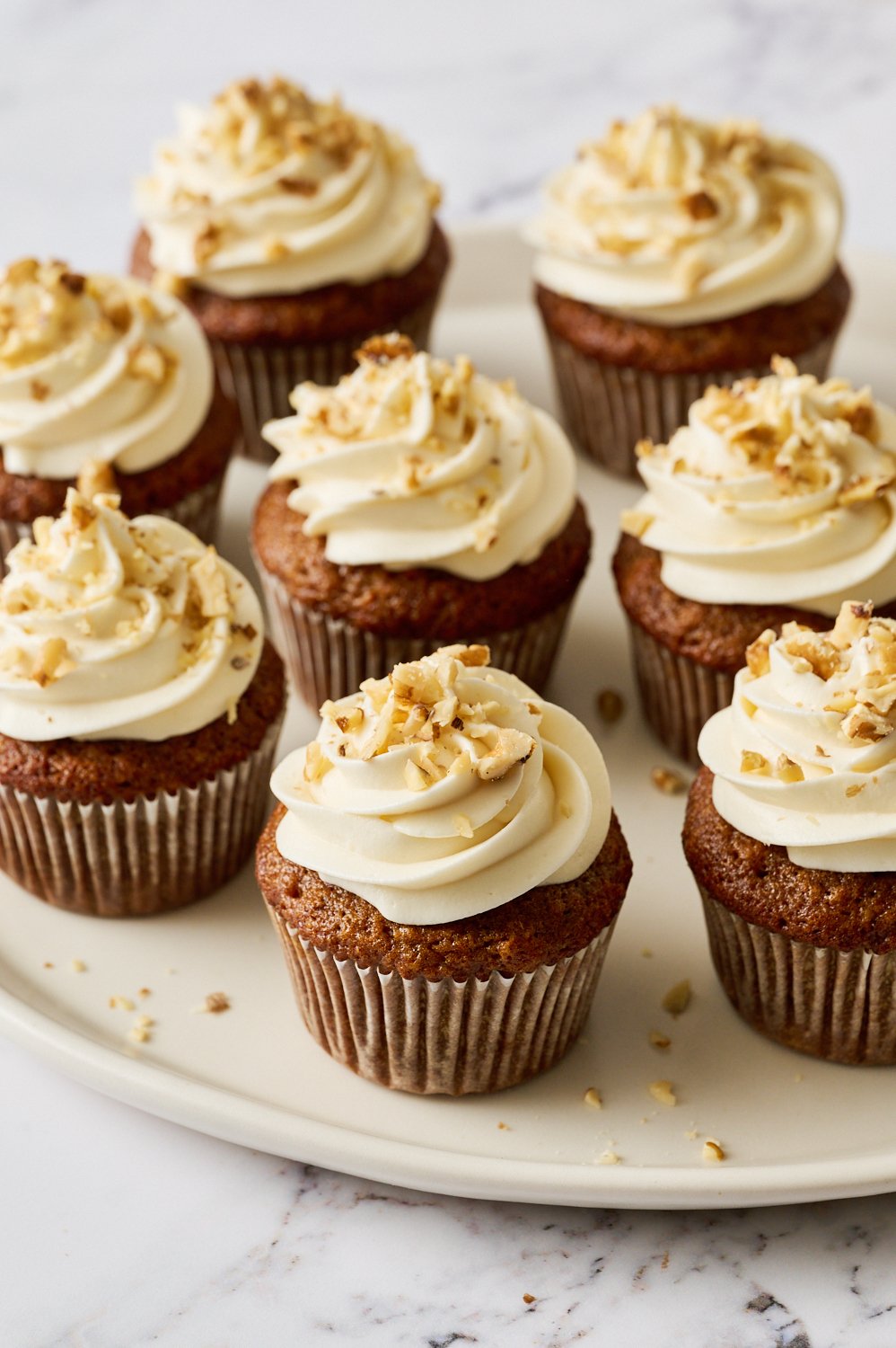 several carrot cake cupcakes iced with cream cheese frosting and garnished with chopped walnuts.
