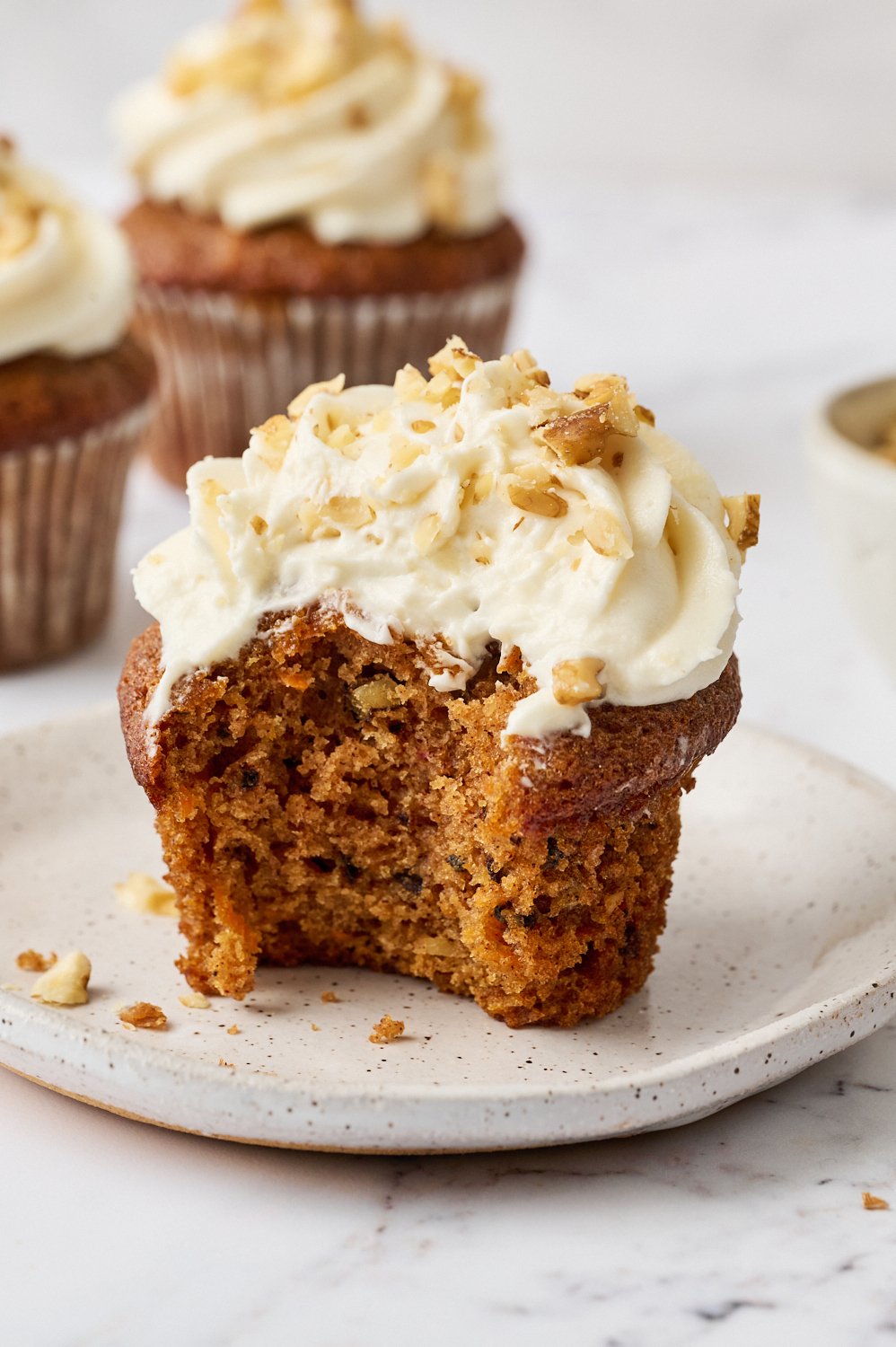 a carrot cake cupcake on a white plate with a bite taken out.