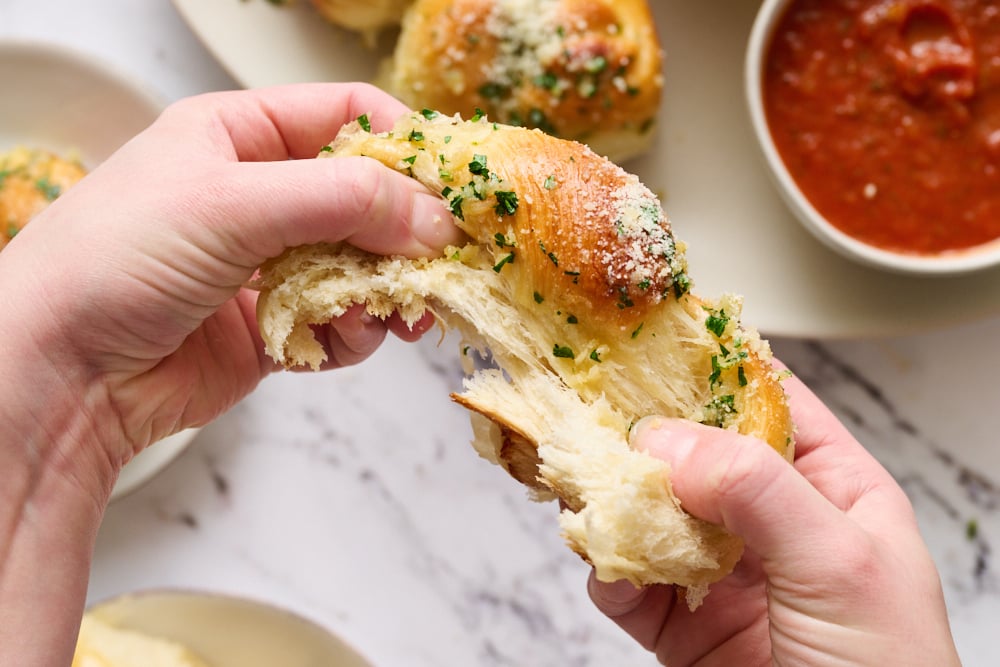 a garlic knot roll being torn in half, showing how soft and fluffy they are.
