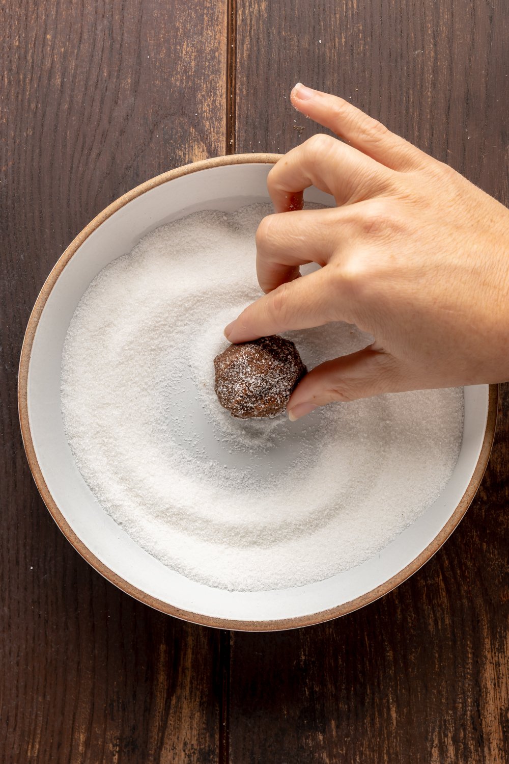 rolling one cookie dough scoop in granulated sugar to coat