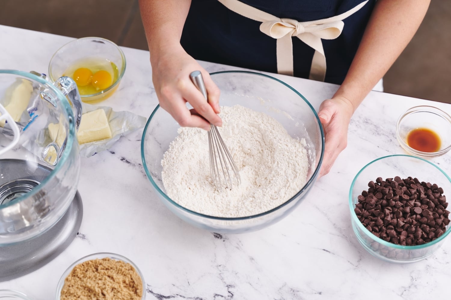 overhead view of Tessa at a marble counter, whisking the dry ingredients together in a glass bowl