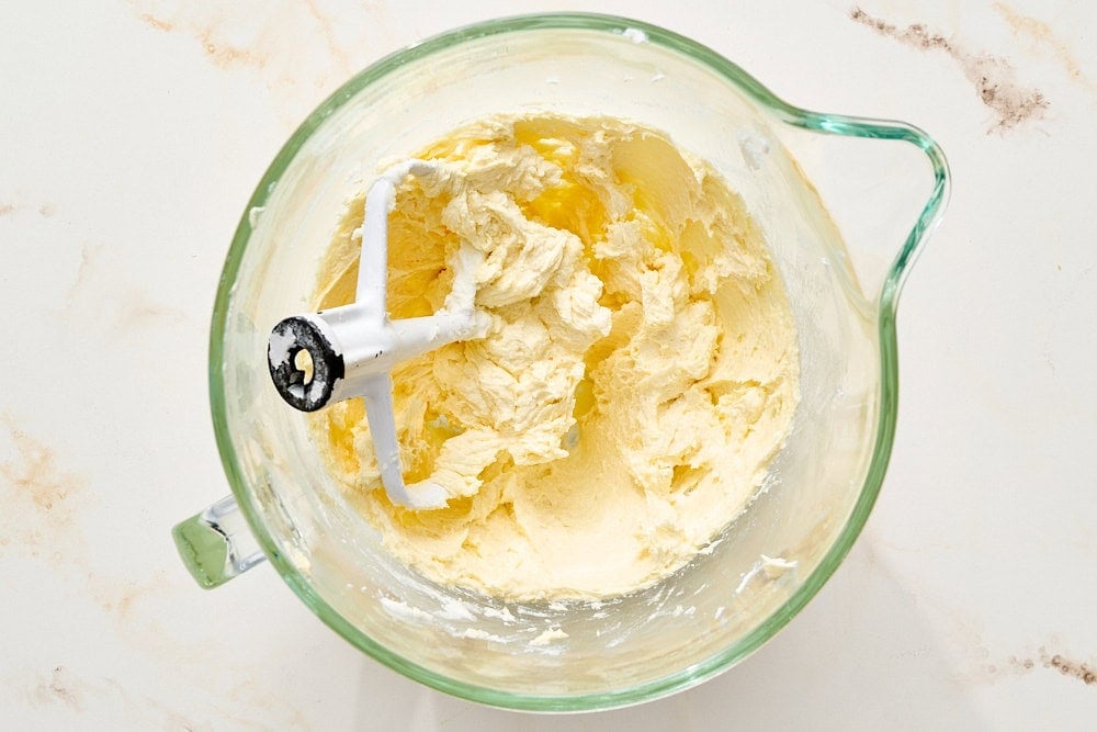overhead view of butter and sugar creamed with eggs added in a glass mixing bowl for sugar cookies