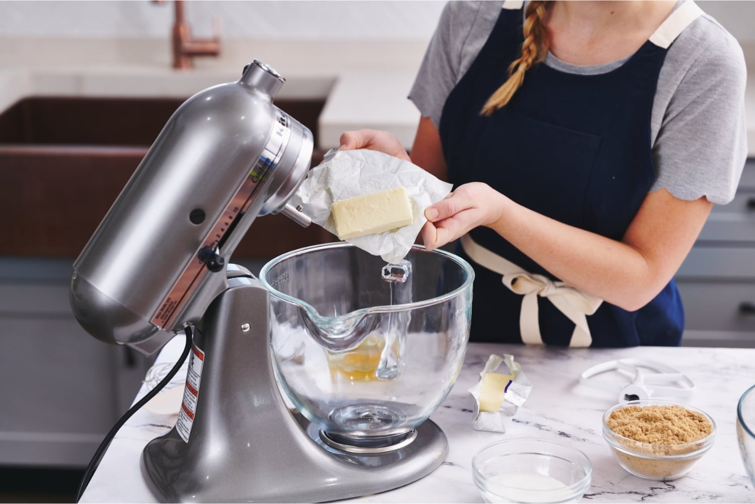 Tessa at a counter with a stand mixer, adding butter to the mixing bowl