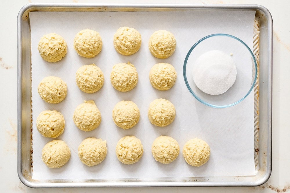 overhead view of sugar cookie dough scoops next to a bowl of sugar for rolling