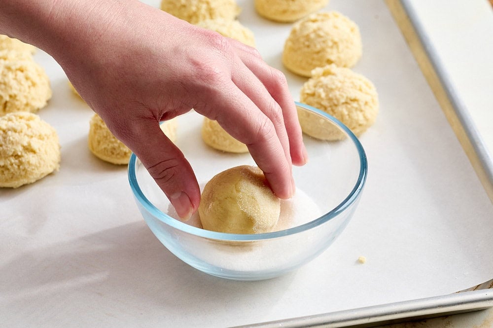 three quarter angle view of a hand rolling a ball of sugar cookie dough in sugar
