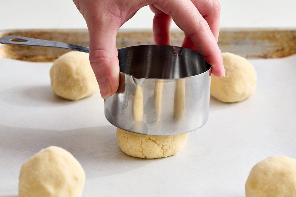three quarter angle view of a measuring cup pressing down a ball of sugar cookie dough just slightly
