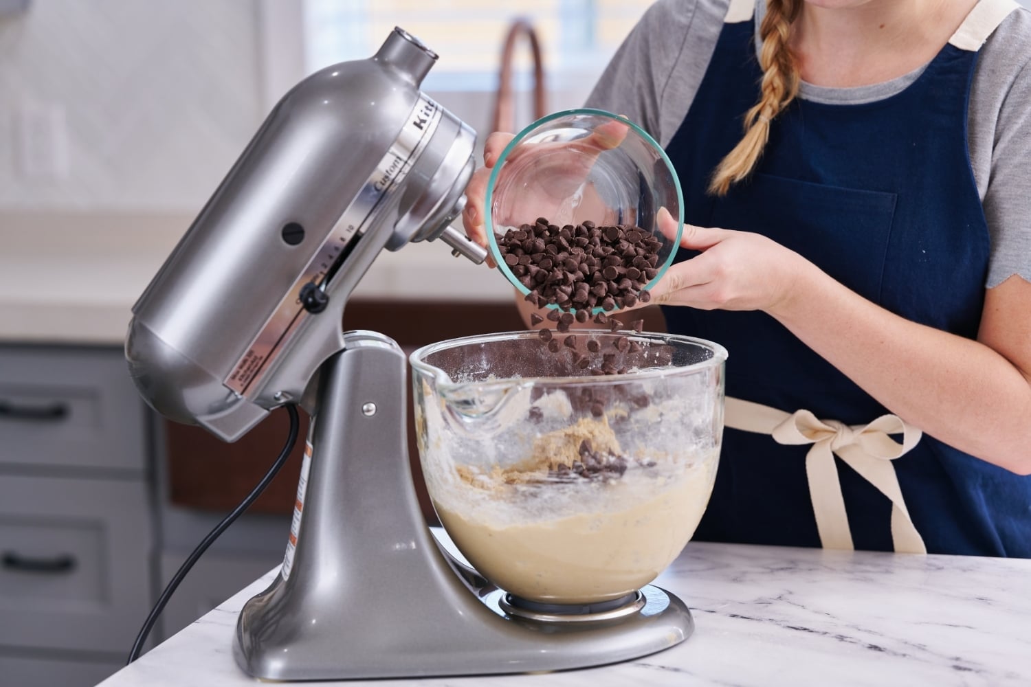 Tessa adding chocolate chips to dough in mixer bowl