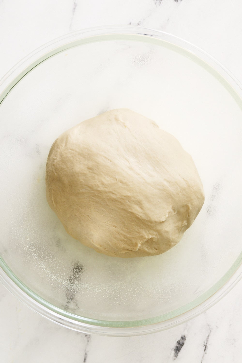 overhead look of pretzel bun dough in a glass bowl before rising