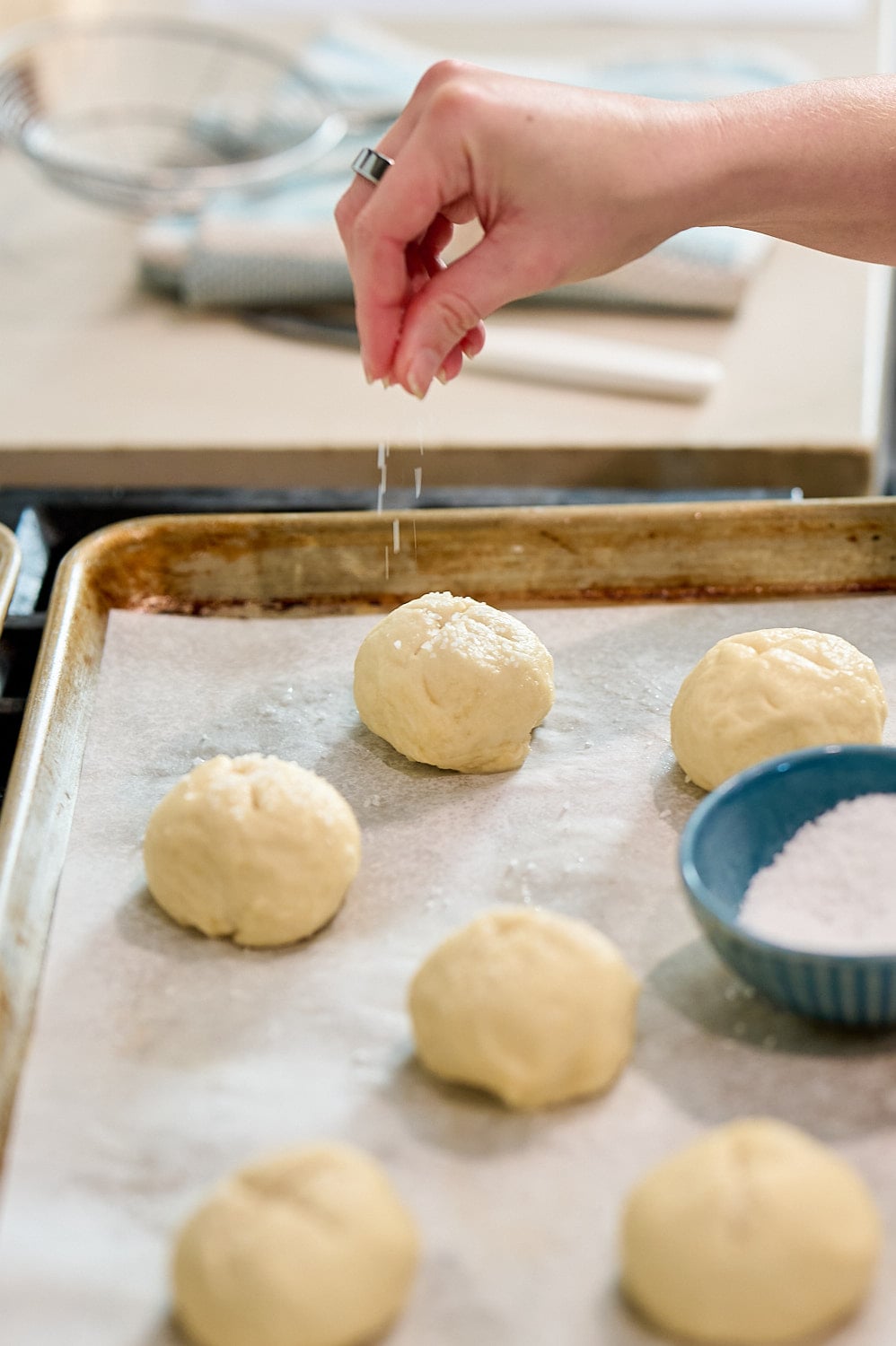 hand sprinkling salt on pretzel buns