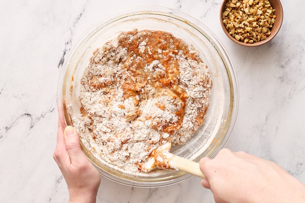 adding dry ingredients to wet ingredients in glass mixing bowl