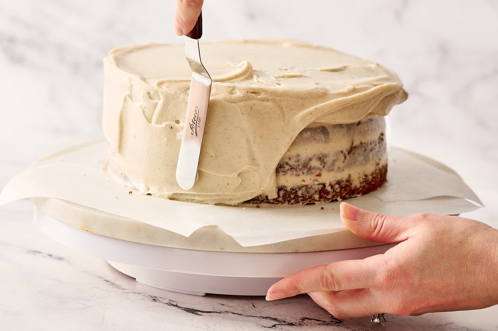 cake on turntable with hands using an offset spatula to frost