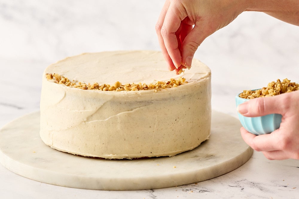 garnishing the frosted carrot cake with a rim of chopped walnuts
