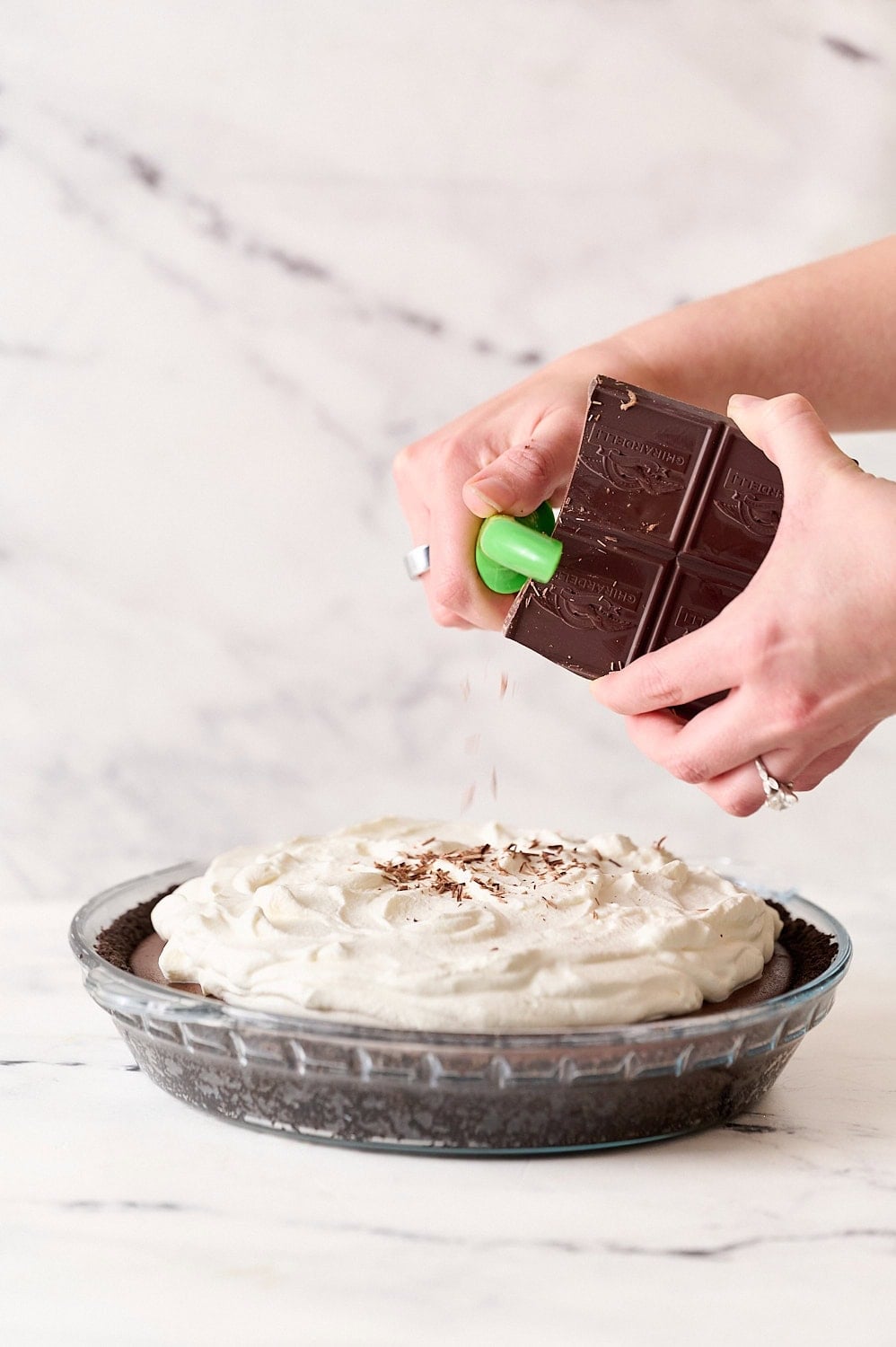 shaving a block of chocolate with a vegetable peeler to create small chocolate curls on top of the pie
