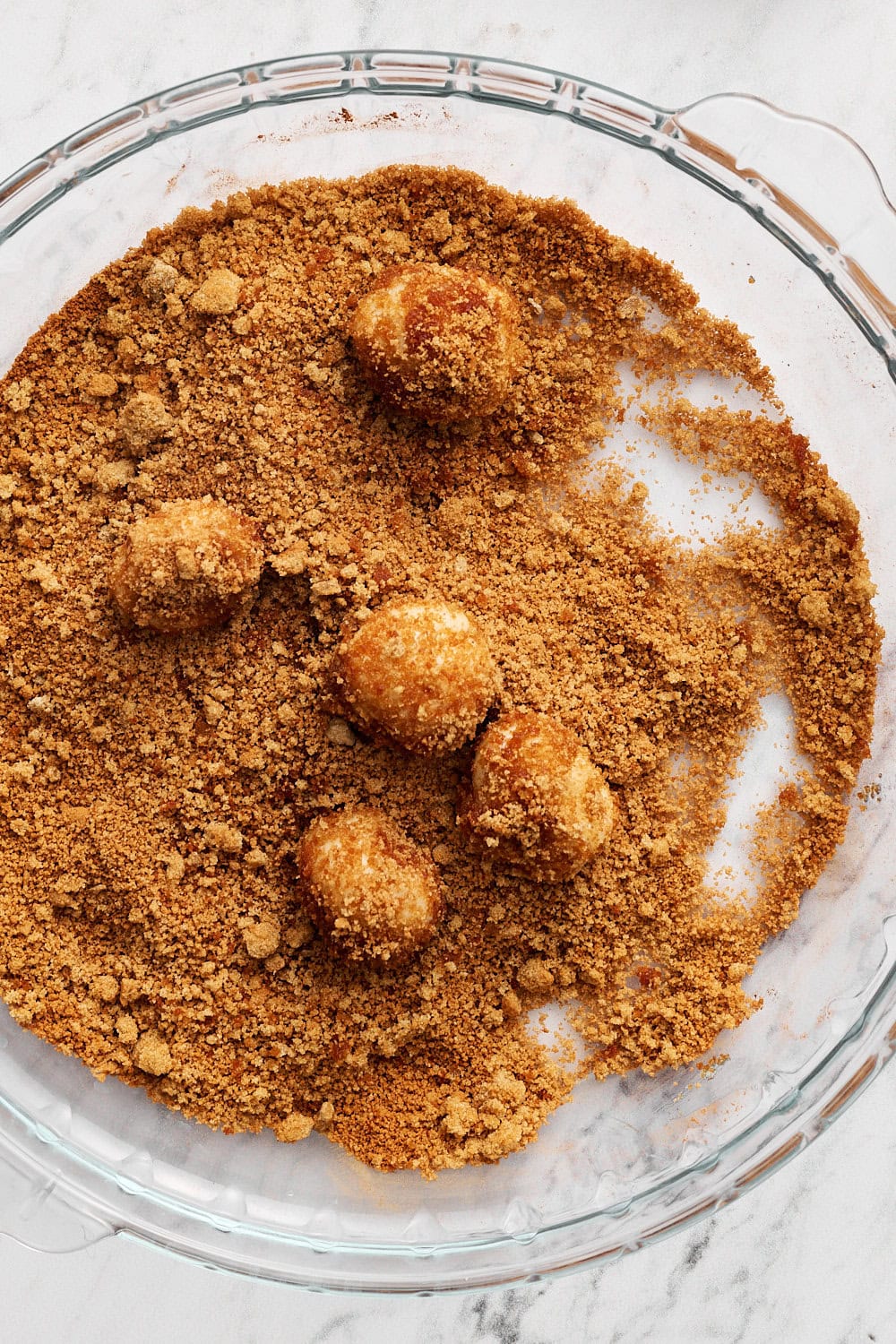 coating balls of dough in a glass pie pan with cinnamon sugar
