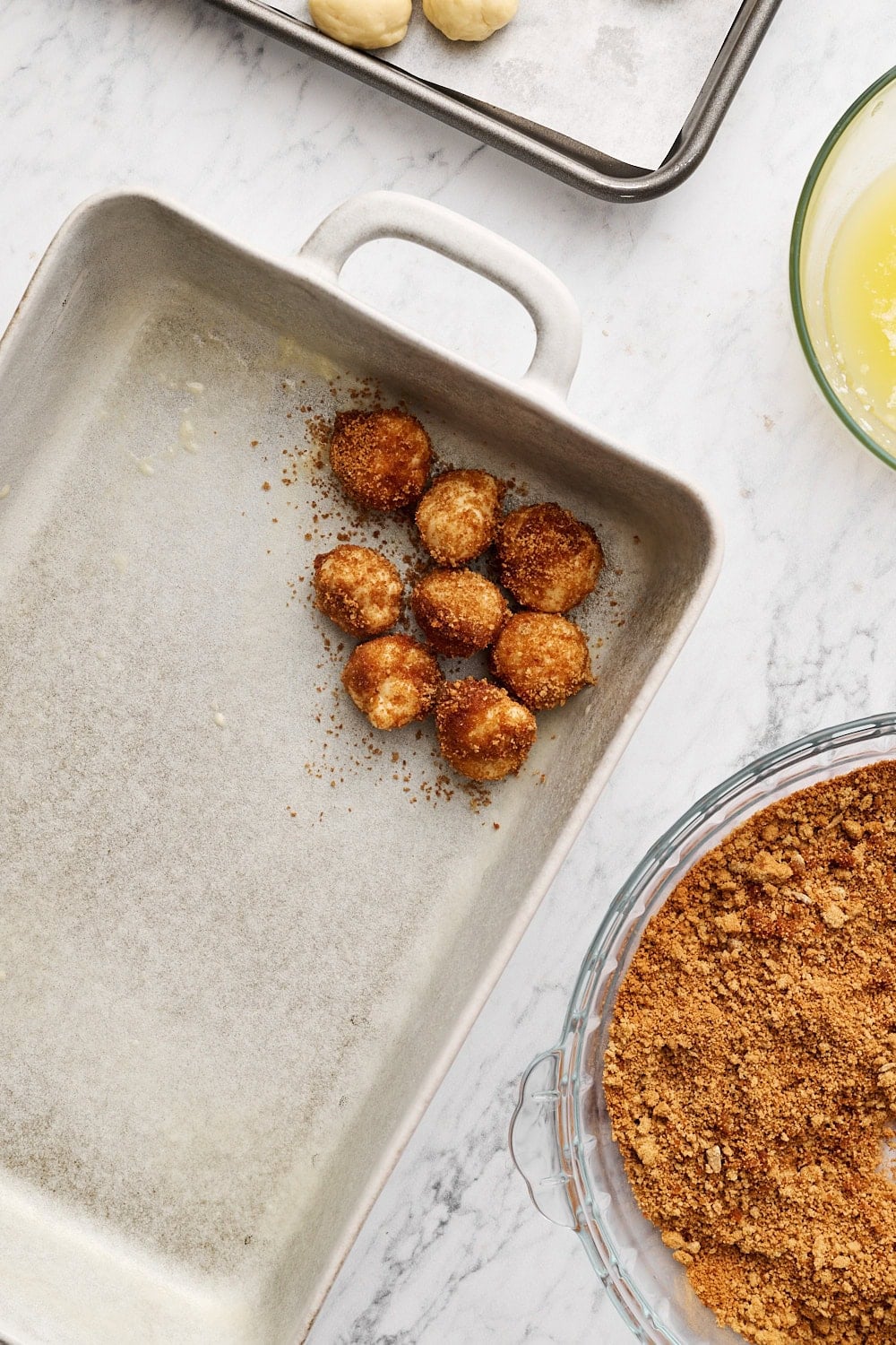 placing coated dough balls into a gray ceramic baking dish on a marble surface